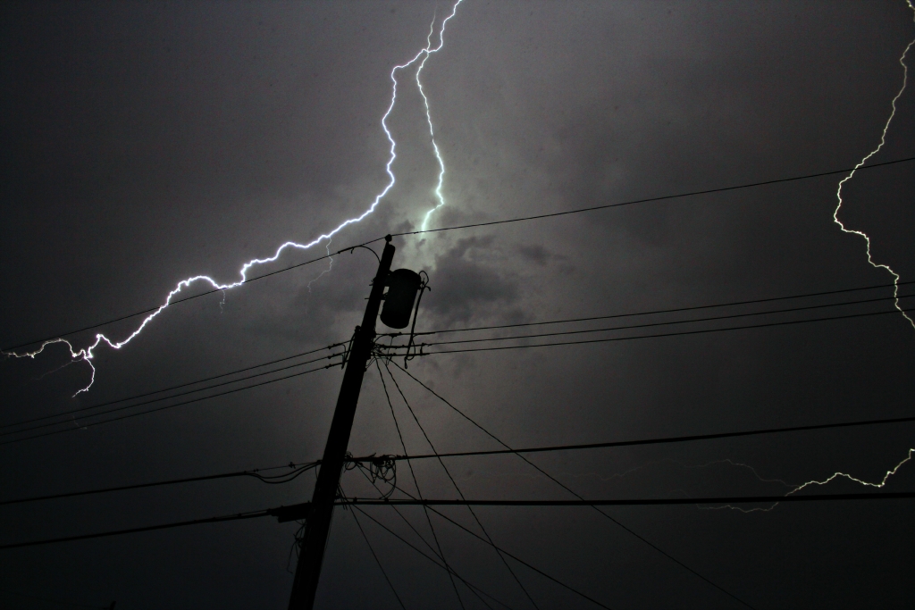 Silhouette of utility poles and wires during a thunderstorm.