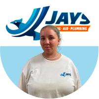 Woman in white shirt with company logo standing in front of a "meet the team" signage background.