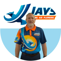 A man in a branded uniform standing in front of a company logo for Jay's Heating Air Plumbing, ready to meet the team.