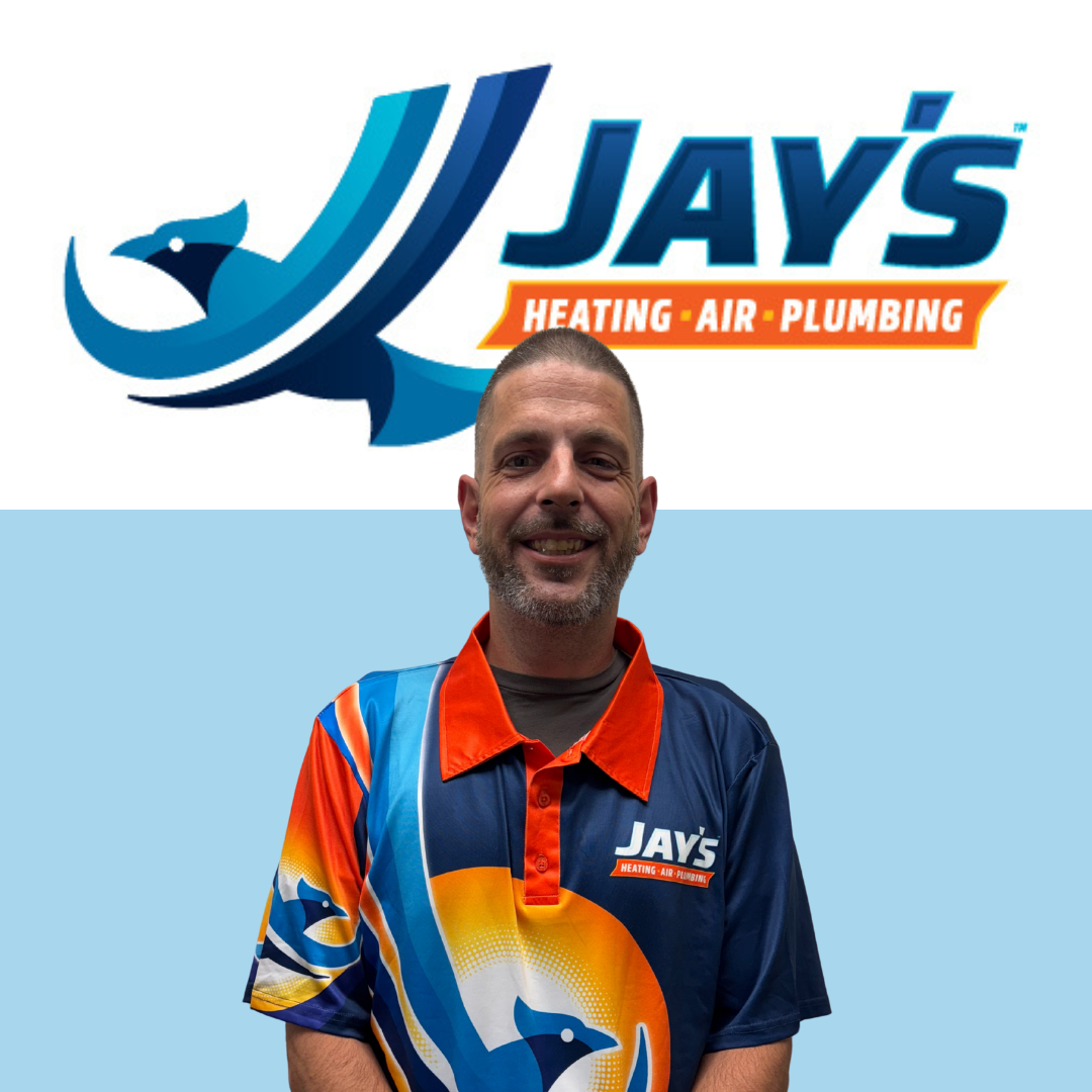 A man wearing a Jay’s Heating, Air, Plumbing shirt stands smiling in front of a Jay’s Heating, Air, Plumbing logo on a blue and white background.